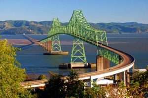 A big green metal bridge crosses a wide river; in the background there are hills with patchy trees for article on soil erosion