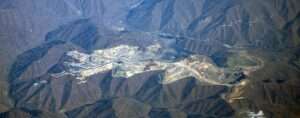 An aerial photo of dark, bare mountains; In the center is a deep pit full of gray stone rubble.